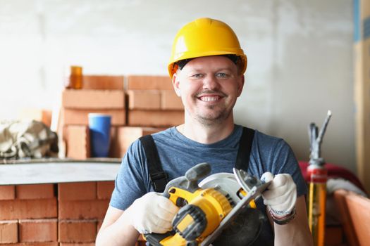 Portrait of happy carpenter worker with professional sander machine get ready to work. Qualified foreman in helmet. Construction site, renovation concept