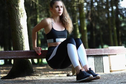 Portrait of serious sweaty girl doing push ups on bench in park, work hard on perfect body. Fitness, sport, physical activity, habit, weight loss concept