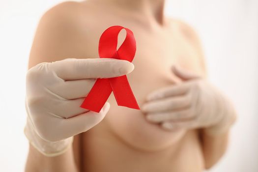 Close-up of woman hold red ribbon in hand wear glove, fight breast cancer, message for female fighting disease. Breast cancer, medicine, diagnostic concept