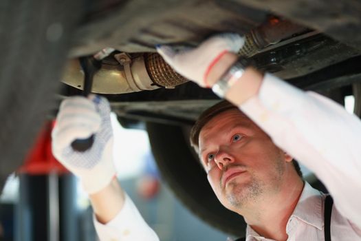 Portrait of automechanic with wrench repair part under automobile, busy handyman at work. Worker fix machine on station. Car maintenance, repair concept