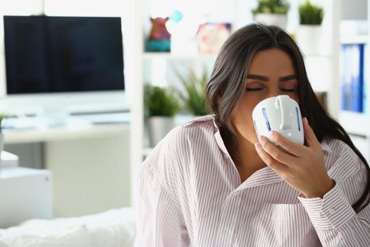 Portrait of lovely sleepy woman drink coffee to wake up in morning, caffeine for energetic day start. Lady in pyjamas at home. Good morning, ritual concept