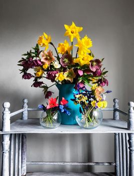 The art of flower arrangement. Romantic bouquet in retro style with flowers daffodils, hellebore, hyacinths, primrose, muscari and tulips on a vintage coffee table in the interior