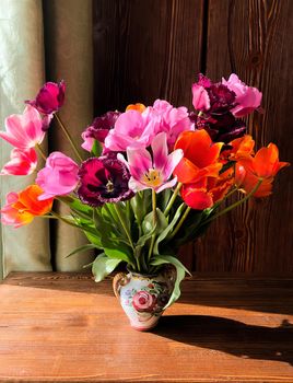 Home decor and the art of arranging bouquets. Spring romantic bouquet with garden colorful tulips in the interior on a wooden table near the window