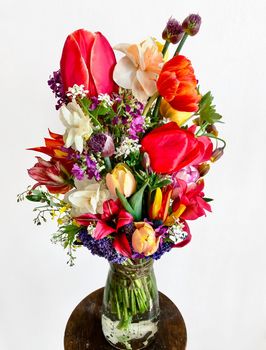 Home decor and the art of arranging bouquets. Bouquet of colorful garden flowers on white background. The composition includes tulips, daffodils, alliums, muscari, lunaria, fritillaria and hellebore