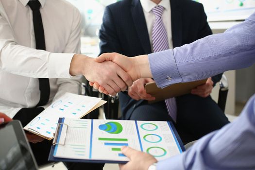 Close-up of partners shake hands over business documentation, beneficial deal. Biz partners perform friendly gesture after conference. Agreement concept