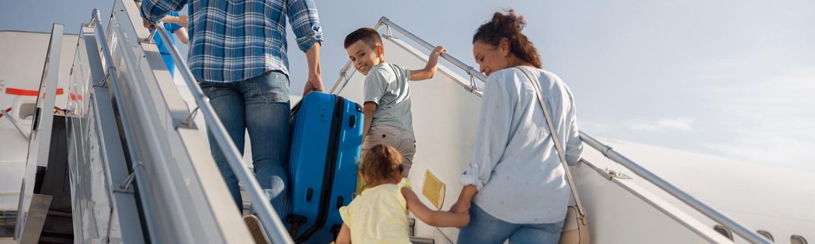 Back view of parents with two kids getting on, boarding the plane on a daytime, ready for summer vacations. People, traveling, vacation concept