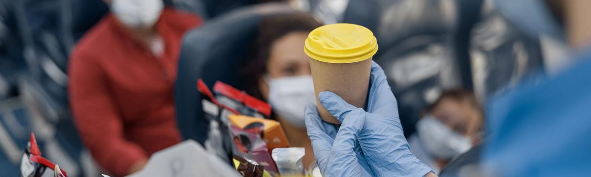 Close up shot of hands in protective gloves of flight attendant serving drinks to passengers on board. Traveling by airplane during Covid19 pandemic. Selective focus