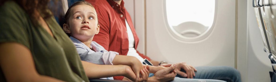 cheerful caucasian family, parents with little daughter holding hands together while sitting on the airplane. Transportation concept