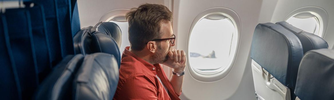 Pensive caucasian man in casual wear resting on the plane, sitting and looking out the window. Relax, travel, vacation, transportation concept