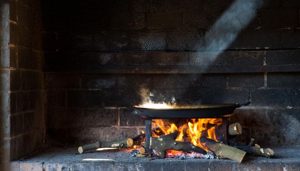 preparing large dish of paella with firewood