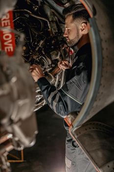 Bearded man aviation maintenance technician checking airplane components while working at repair station