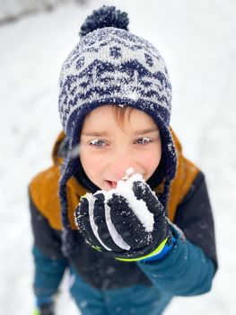 Portrait of a happy five year old boy in the snow in winter. Tastes the snow. Snow on the hat, eyelashes and mittens