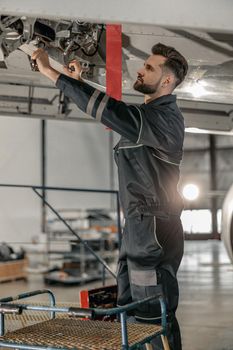 Bearded man maintenance technician tightening bolt with wrench while repairing airplane in hangar