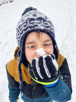 Portrait of a happy five year old boy in the snow in winter. Tastes the snow. Snow on the hat, eyelashes and mittens