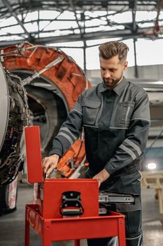 Male worker maintenance technician using tool box while repairing airplane at repair station