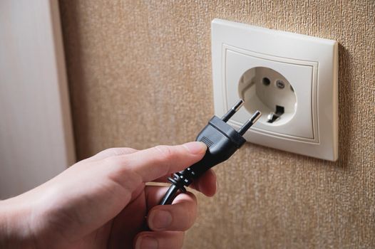 A woman's hand inserts an electric plug into a socket, close-up.