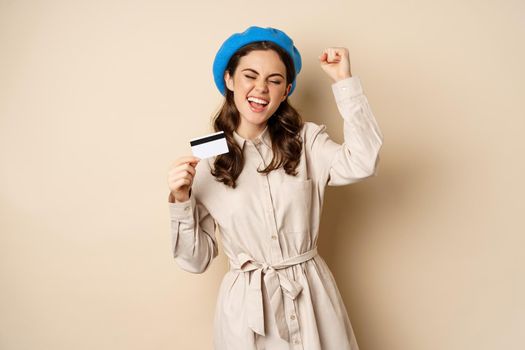 Enthusiastic young woman yearning to go shopping, dancing with credit card and celebrating, laughing and smiling.