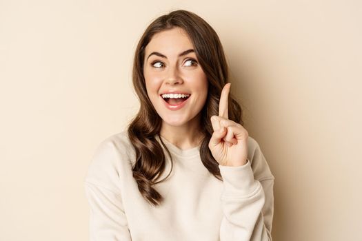 Close up shot of excited woman looking amazed with opened mouth, standing over beige background. Copy space