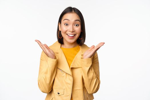 Image of asian woman looking surprised, amazed reaction, shocked face, standing over white background. Copy space
