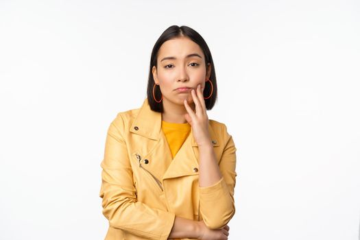 Image of stylish japanese girl looking with unamused, tired and upset face expression, standing in casual clothes over white background. Copy space