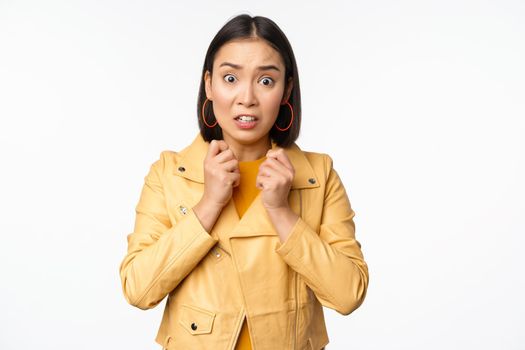 Image of scared asian woman looking insecure and worried at camera, gasping shocked, standing worried against white background.