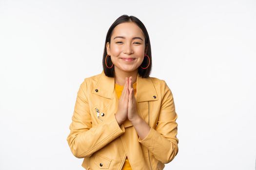 Happy korean woman, looking hopeful, asking for help favour, begging, standing with namaste gesture and smiling, standing over white background.