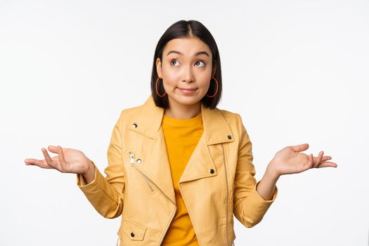Image of korean girl shrugs shoulders and looks confused, dont know, cant tell, standing over puzzled over white background.