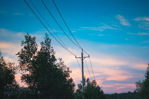 High voltage power pylon transmission huge metal concrete pole of overhead power line energy electric wires outdoor. Industrial Technology and nature in harmony. Sunset evening sky forest background.