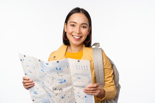 Tourism and backpacking. Smiling asian girl holding map and backpack, tourist searching way, travelling, standing over white background.