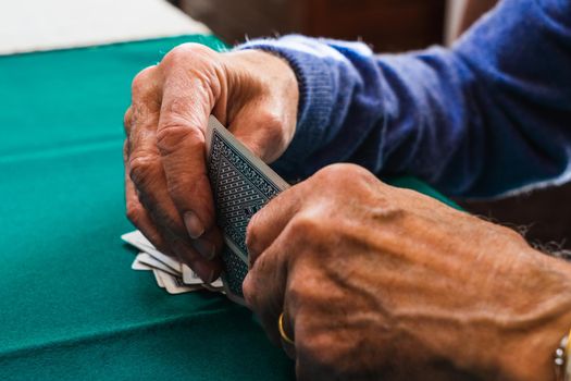 Grandfather's hands playing a card game. Playing cards on a green mat. At the table at home, with natural light from the window. Zenithal shot of hands