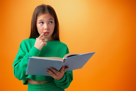 Portrait of clever teen girl with books against orange background in studio