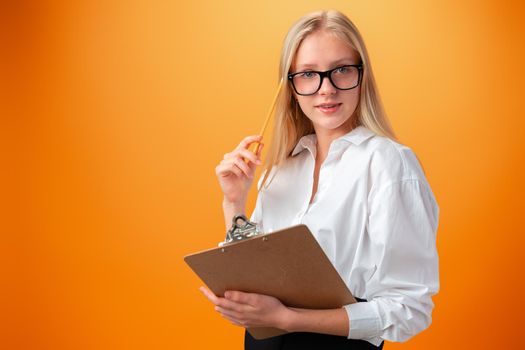 Teen school girl taking notes on clipboard against orange background, close up
