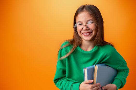 Portrait of clever teen girl with books against orange background in studio