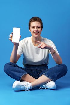 Happy woman shows blank smartphone screen against blue background, close up