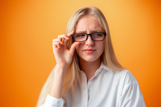 Funny caucasian teen girl in eyeglasses isolated on orange background, close up