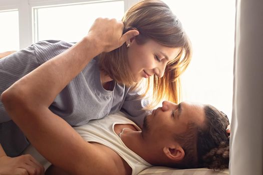 Portrait of a multiracial couple, boyfriend and girlfriend face to face, lie near the window.