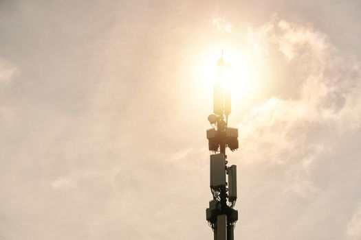 Telecommunication tower of 5G cellular. LTE radio network communication equipment with wireless modules and smart antennas mounted on metal pillar on clouds and sun sky background.