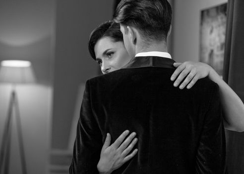 Dancing passion woman hugs man standing back to camera. Husband and wife after a romantic dinner. Romance in relationships. Beautiful young couple in home interior. Black and white photo.