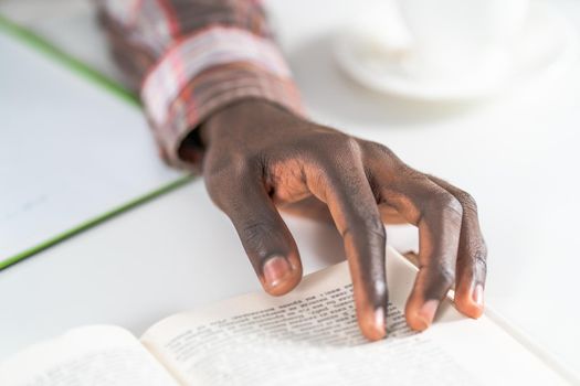 Close up on young male hand of african american man reading book making notes. Student preparing to the lecture at library reading books and making notes. Adduction concept.