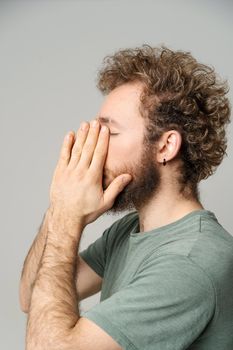 Young curly haired man hide face in hands tired, migraine concept. Handsome guy feel pain or headache. Frustrated young man trying to concentrate massaging his face. Health care concept.