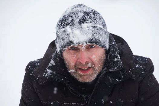 Portrait of a positive man in a black hat in the snow close-up with an open mouth. Close-up of the climber's face.