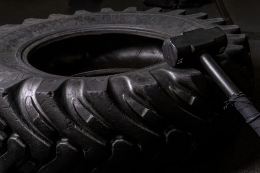 A tire on a black background with a sledgehammer lies for crosfit fitness wheel sledgehammer workout body sport, for fit gym for strength concentration physical, flip build. Equipment indoors up,