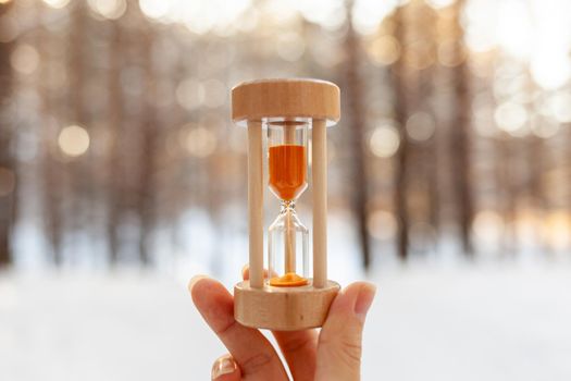 Winter is coming. Hourglass in the snow. sandglass Hourglass as a symbol of changing of the seasons. Spring is coming. melting snow. Hourglass in a woman's hand in a snowy forest in winter