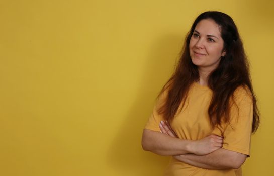 Beautiful woman in yellow t-shirt with long dark hair on yellow paper background. Pleasant brunette on a yellow background.