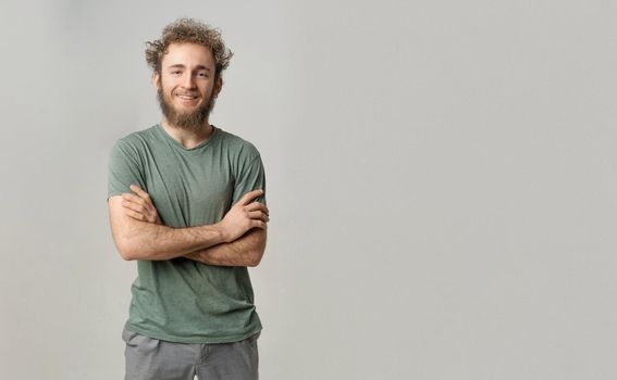 Handsome smiling young handsome bearded wild curly hair man with bright blue eyes isolated on white background. Young thinking man in green tshirt on white background.