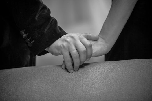 Close up on hands of beautiful young couple in home interior. Romance in relationships, love and tenderness. Husband and wife after a romantic dinner. Black and white photo.