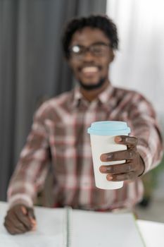 Selective focus on African american man hand with cardboard cup or disposable cup for coffee or tea. White disposable cup with blue plastic lead in mans hand. Disposable dishes concept.