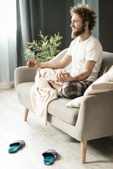 Handsome man sitting on the couch or sofa at home, enjoying meditation in his pajamas in living room during lockdown or being sick or weekend relax.