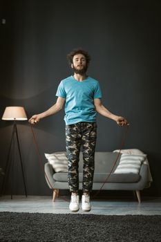 skipping rope jumping young man working out at home. Young man on self isolation or quarantine, pandemic days. Handsome curly hair man use skipping rope to stay fit and healthy.