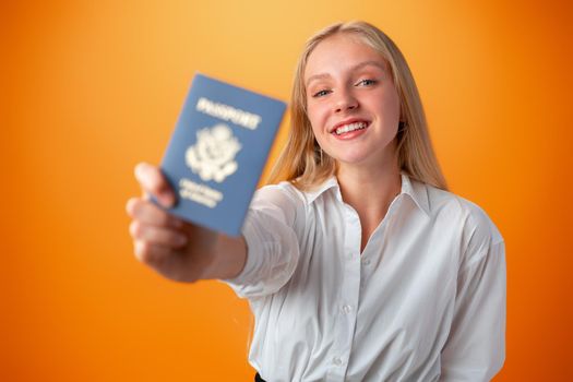 Teen girl holding passport to travel against orange background in studio